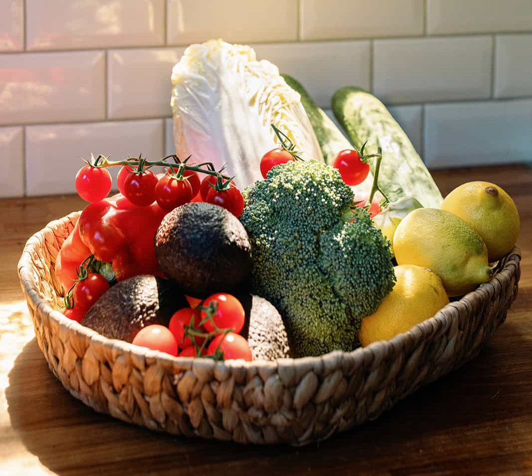 Basket of fresh fruits and vegetables on a wooden table with a tiled wall background