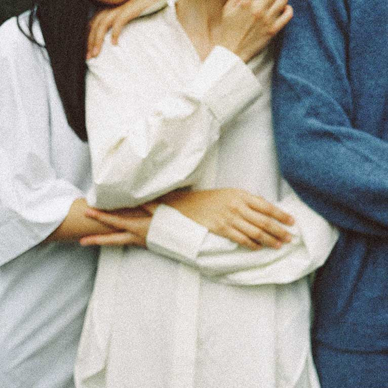 Two people embracing, one in a white outfit and the other in a blue outfit.