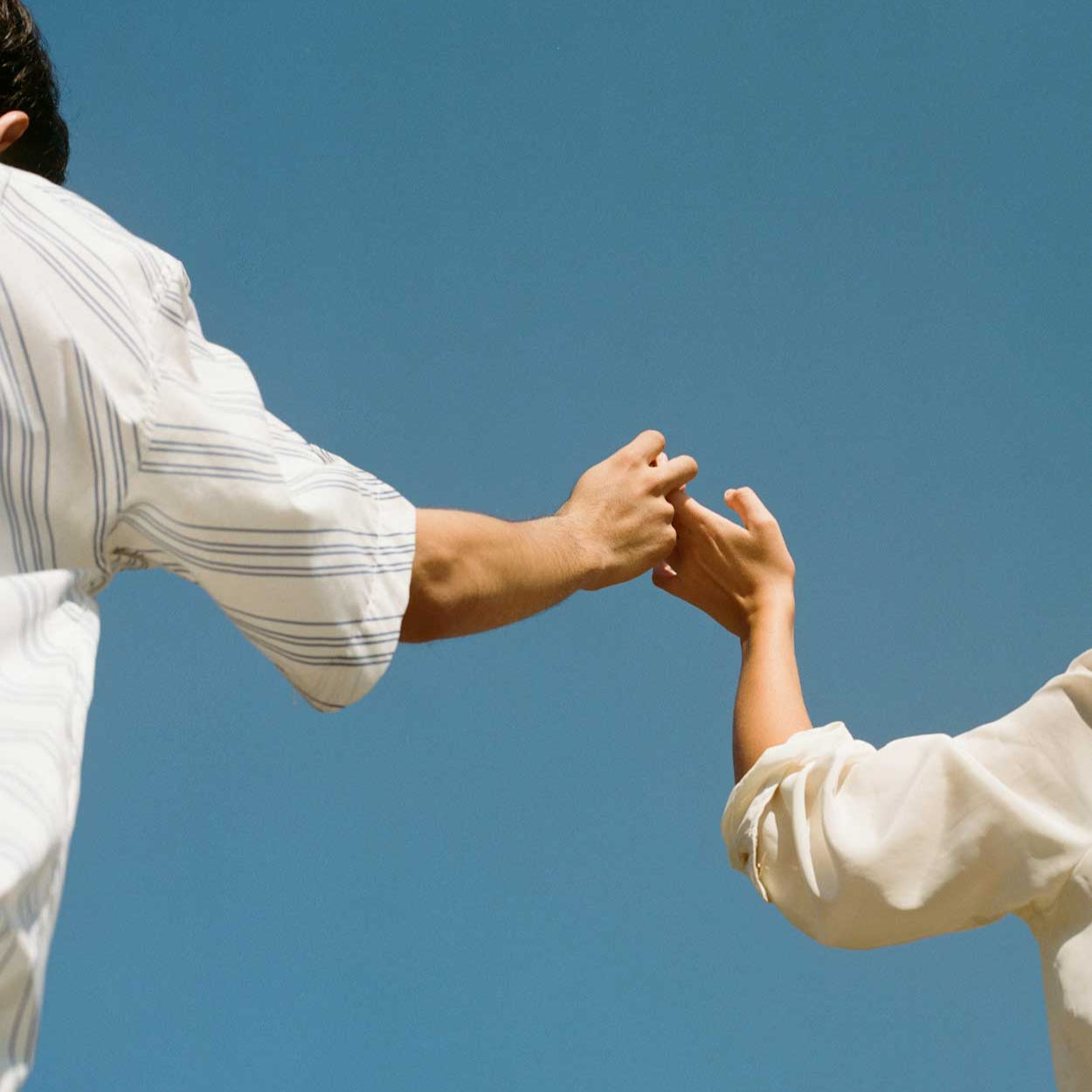 Two people holding hands against a clear blue sky.
